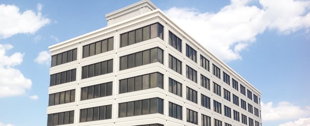 The top four stories of a white office building with black windows. A blue sky with fluffy white clouds is in the background. 