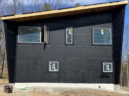 A two-story home under construction. The exterior walls are covered with a black weather barrier.