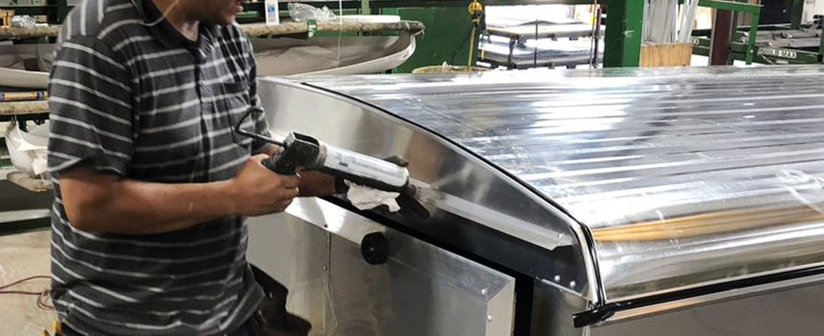 fabricator applying sealant around a cargo trailer in a factory