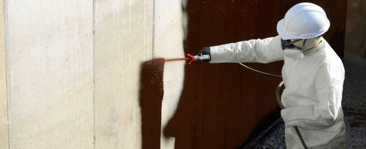 man spraying waterproofing membrane on exterior wall